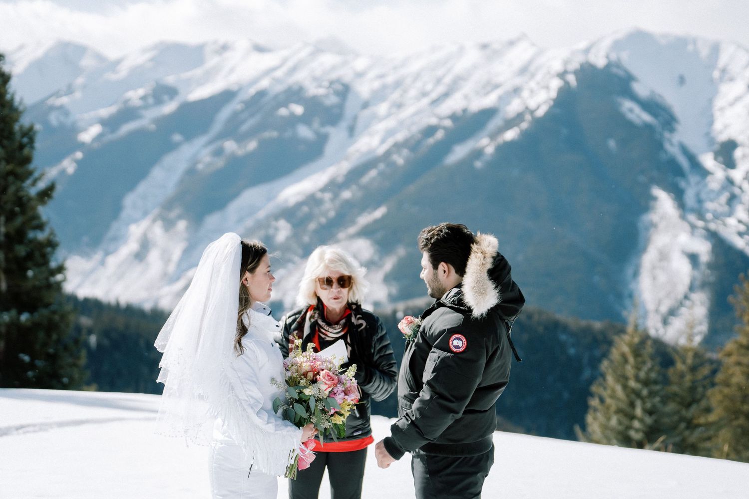 Three people stand in the snow with majestic snow-capped mountains in the background.