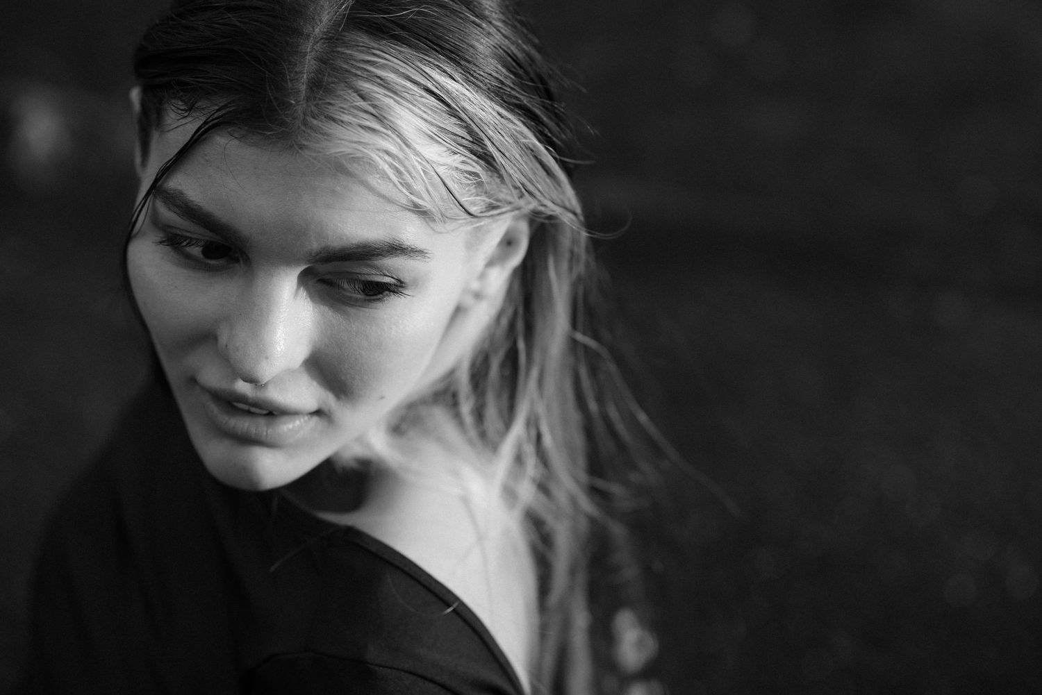 Black and white portrait photograph showing a candid profile view of a person with blonde hair looking down and smiling.