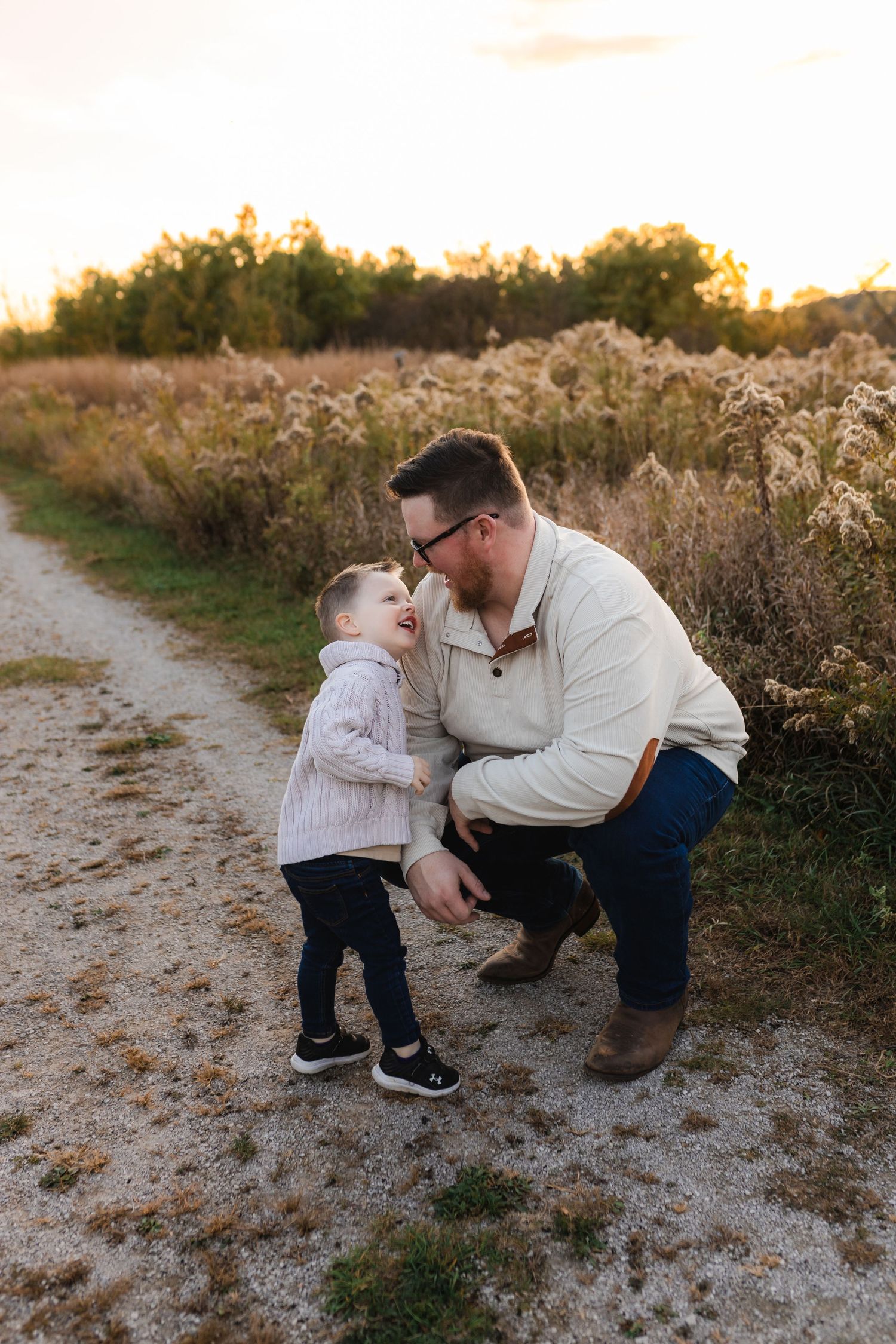 A tender moment shared between a father and son on a dirt path at sunset with tall grass and golden light in the background.