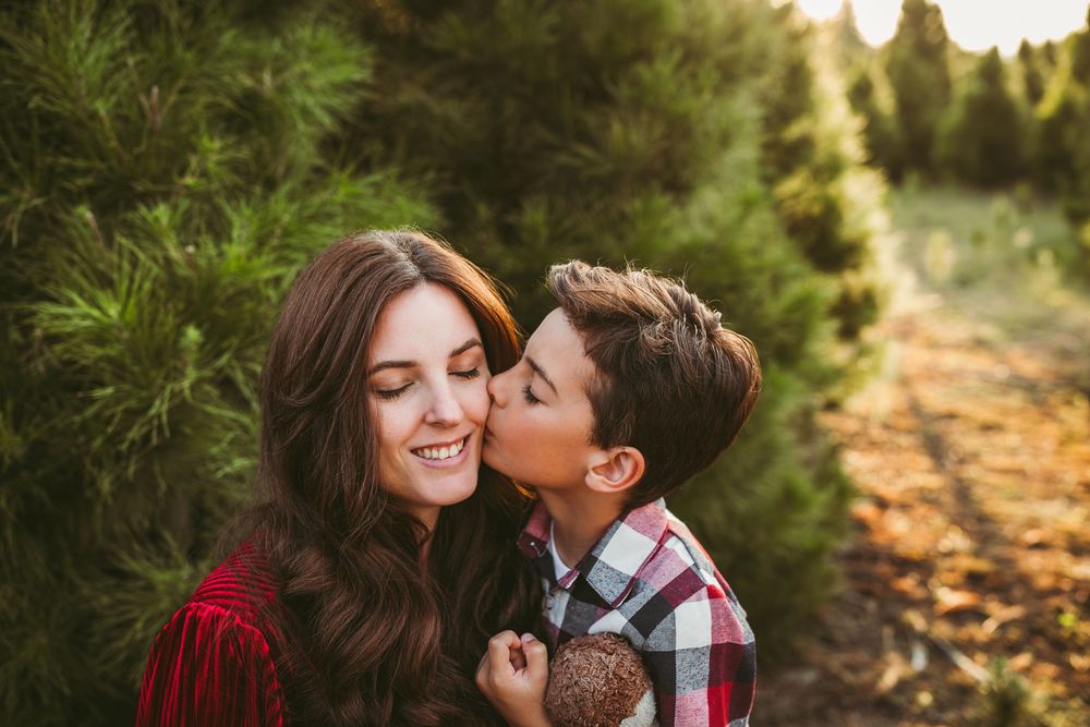 A child in plaid shirt shows affection outdoors among evergreen trees during golden hour.