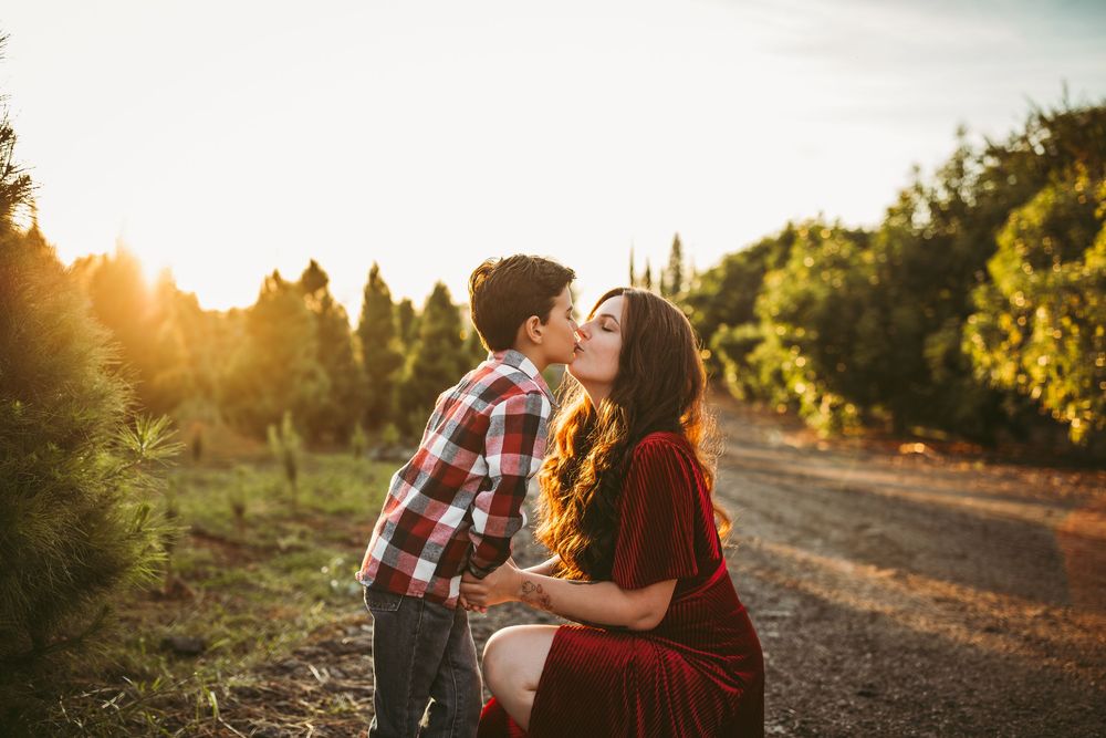 A tender moment between two people sharing affection on a dirt path at golden hour with trees in the background.