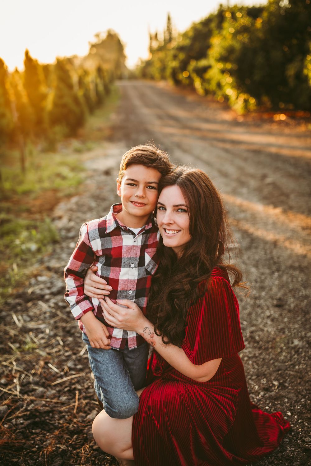 Parent and child in coordinating red outfits pose on dirt road during sunset.