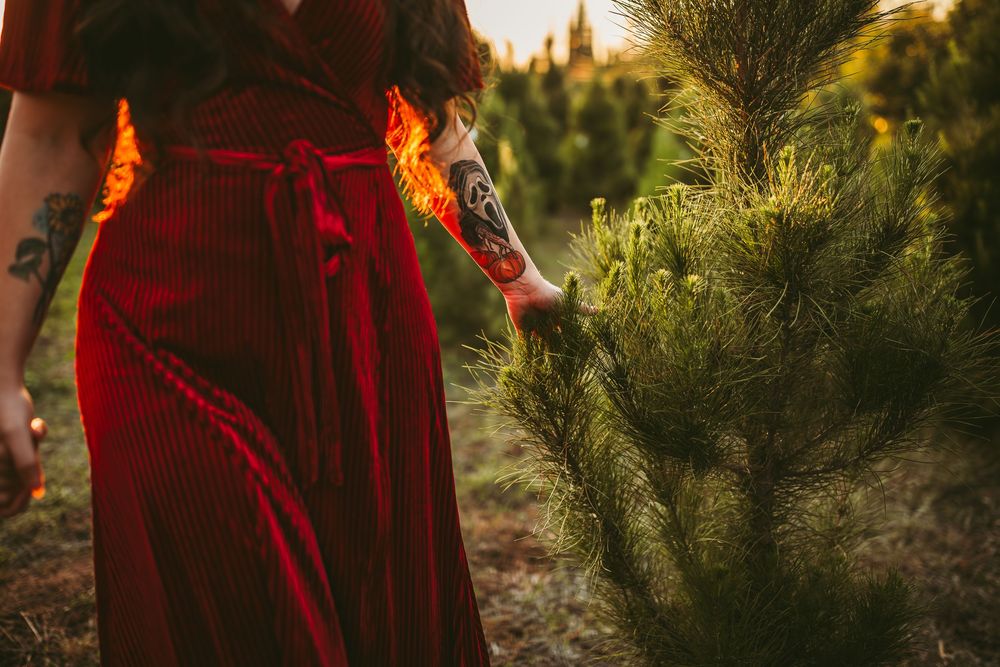 Red-haired figure poses against golden sunlit evergreen trees during sunset photo session.