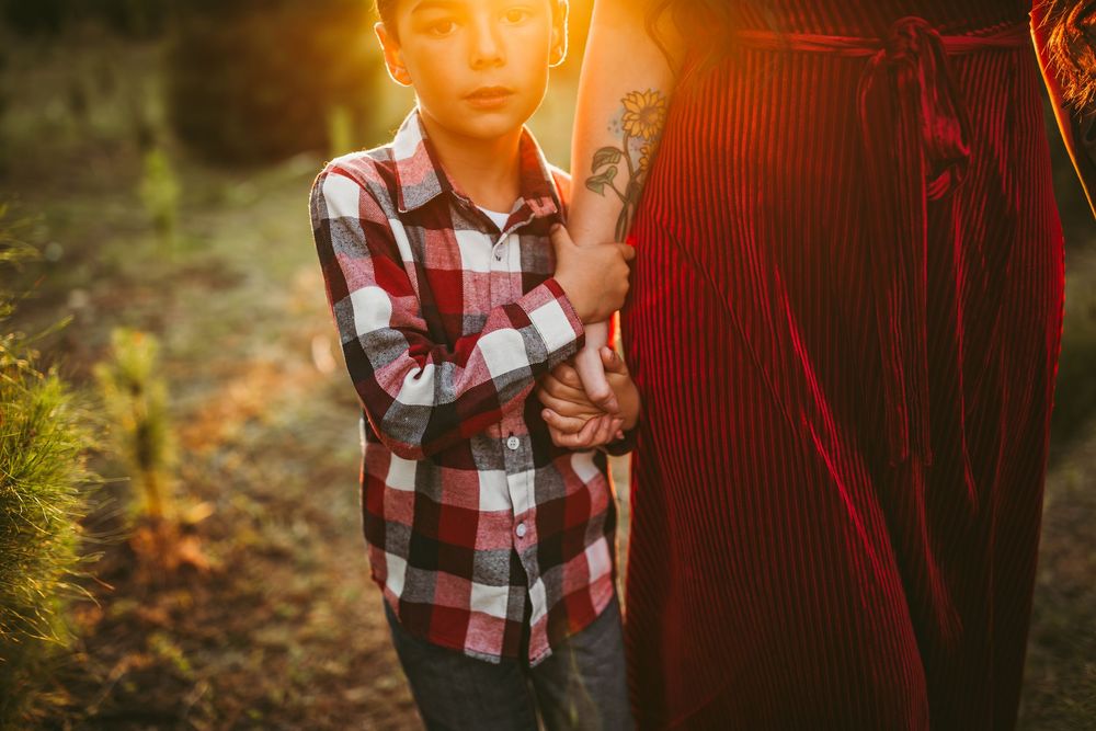 Mother and child share tender moment in autumn forest during golden hour photography session.