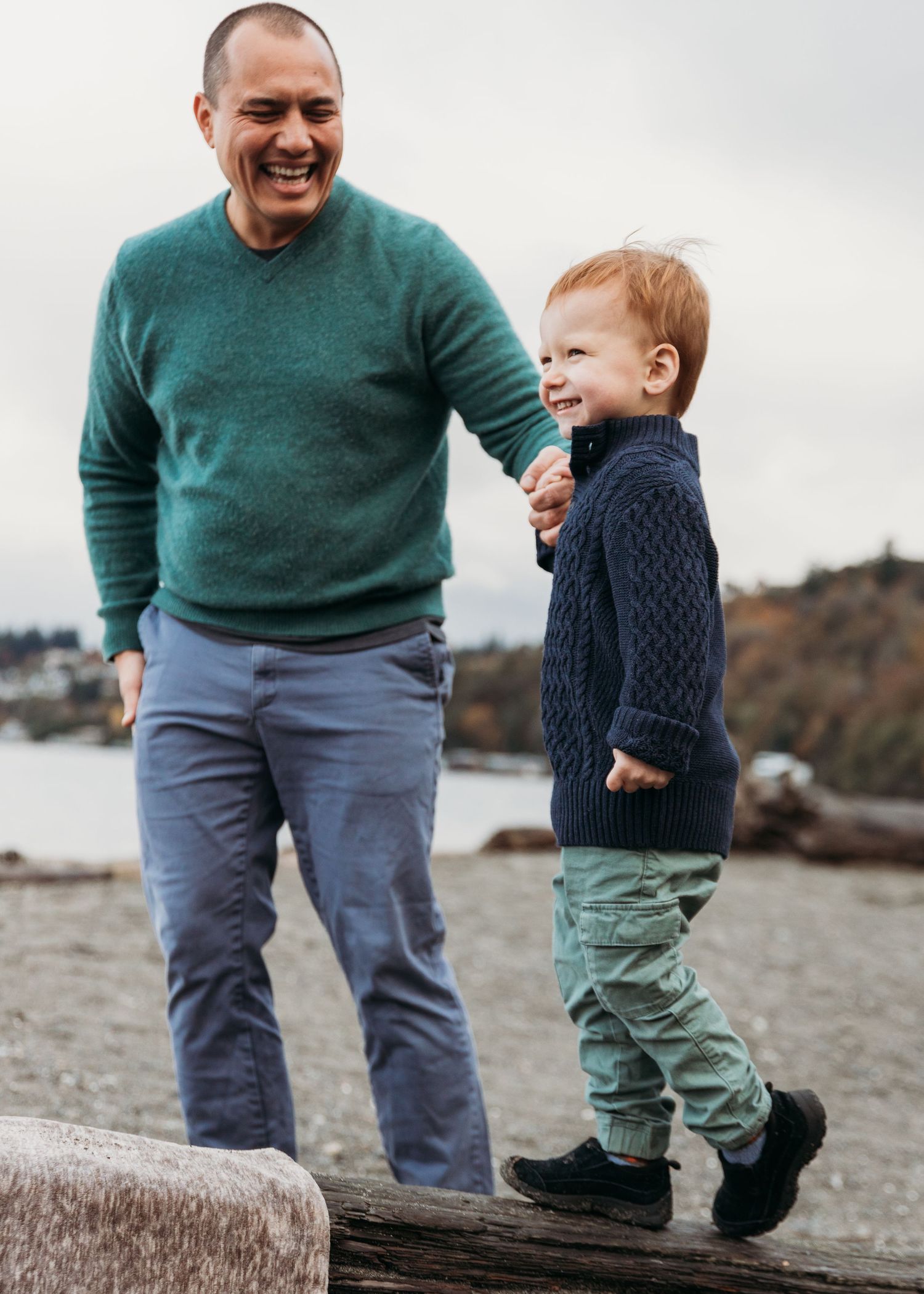 A parent and toddler share a joyful moment walking together on a rocky beach.