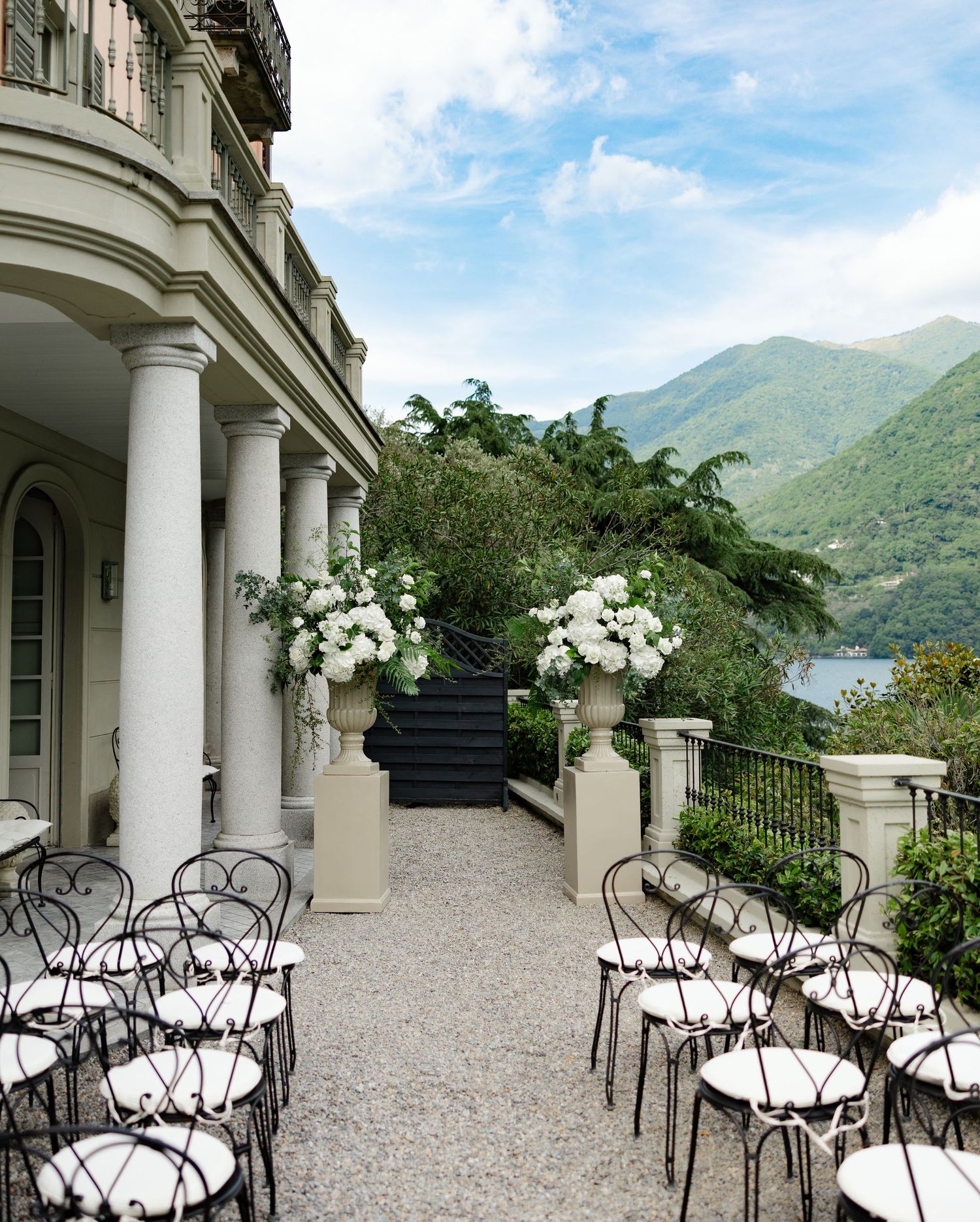 Elegant outdoor terrace with white columns and ornate wrought iron chairs overlooking a scenic mountain lake view.