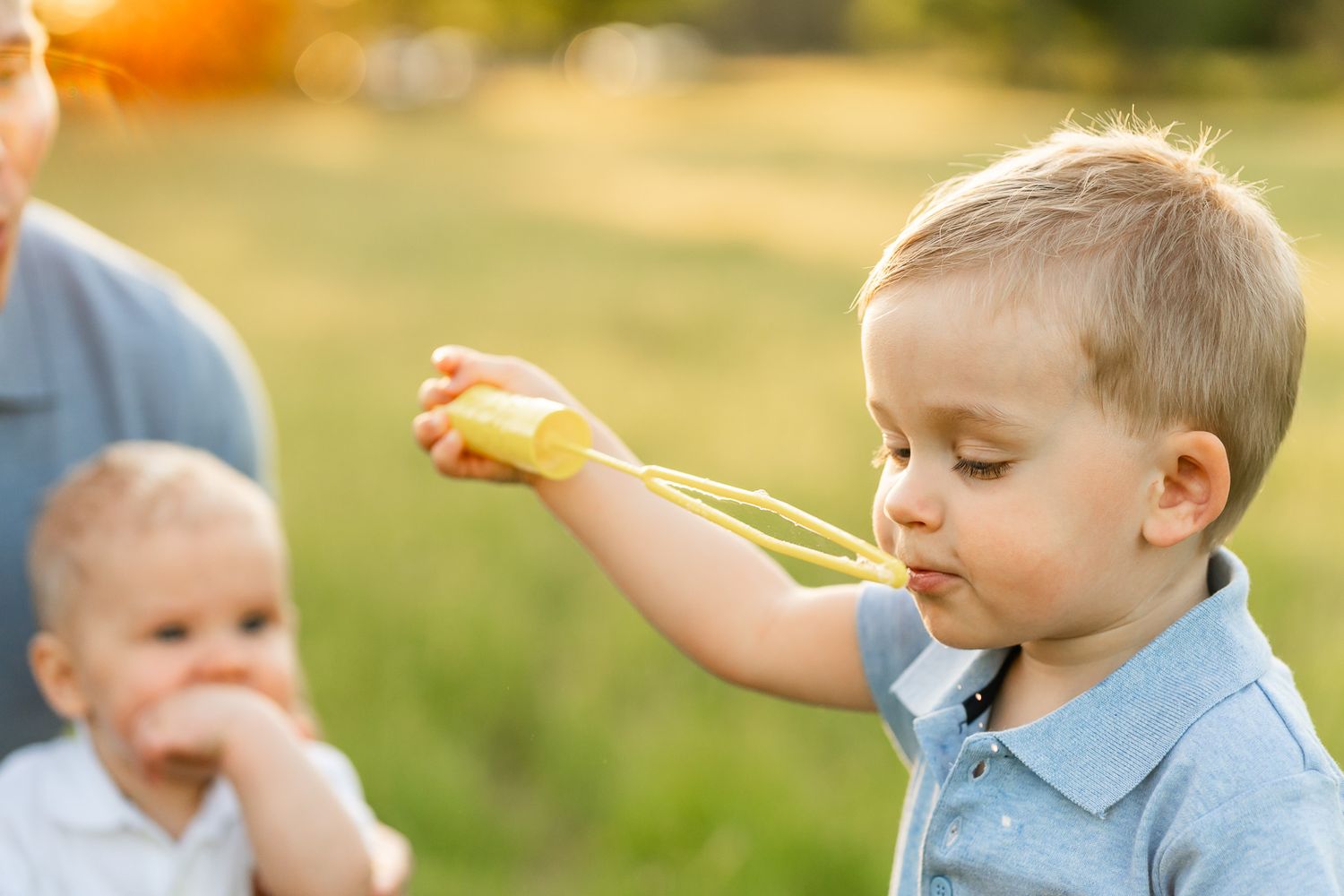 Boy blows bubbles while baby brother looks on.