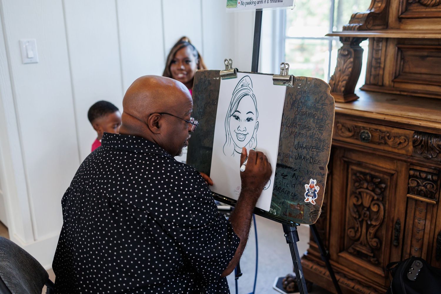 An artist in a polka dot shirt draws a caricature on an easel at a first birthday party at Bella Cavalli