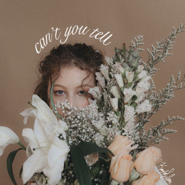 Someone holding a lush bouquet of white lilies, baby's breath and lavender against a warm brown background.