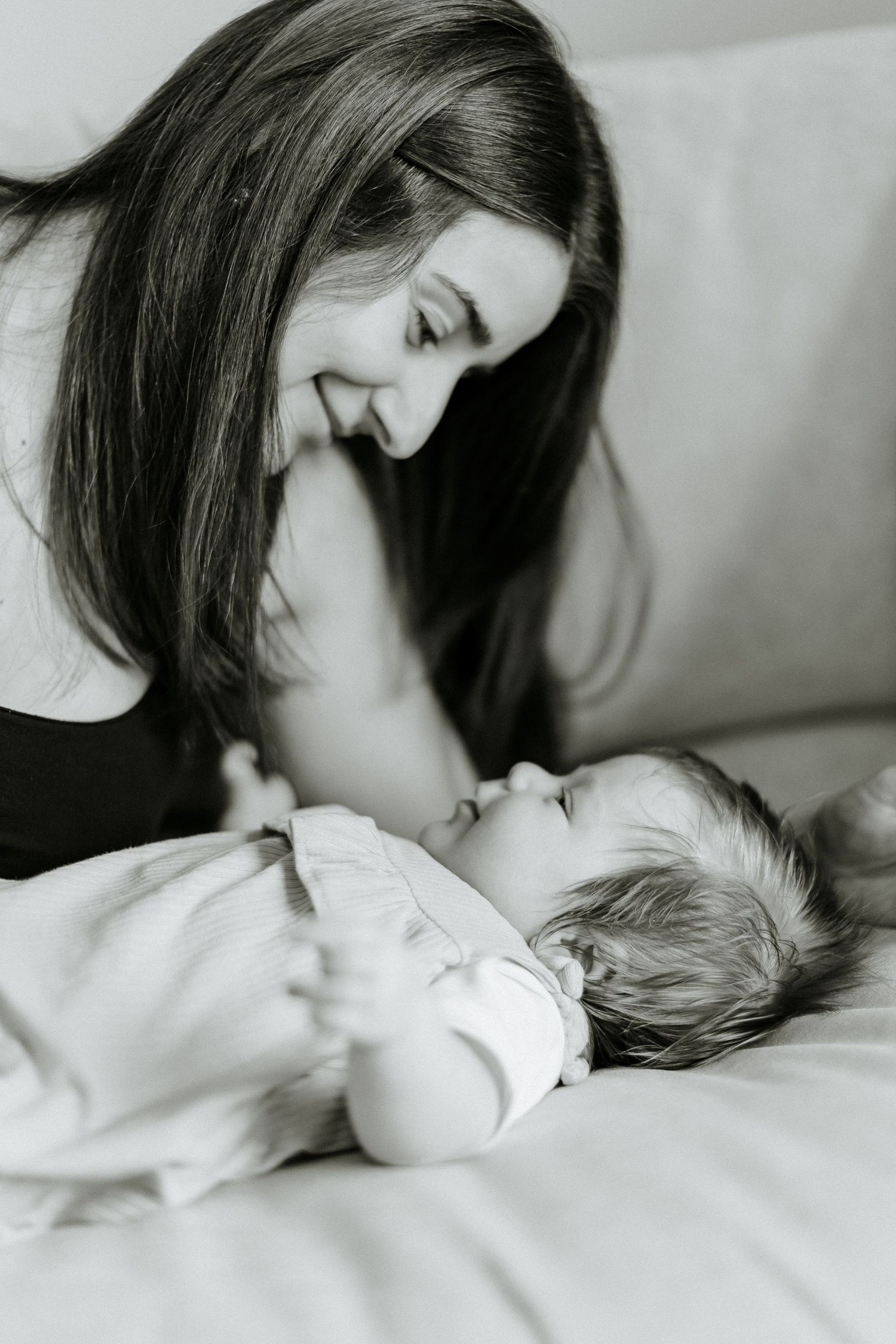 A tender black and white moment captured between parent and sleeping baby on white bedding.