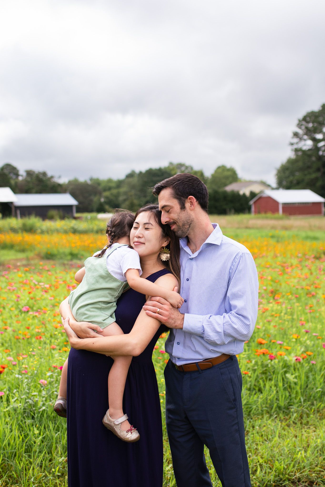 Family shares loving moments together in a vibrant wildflower field with red and yellow blooms on an overcast day at Juniper Creek Farm