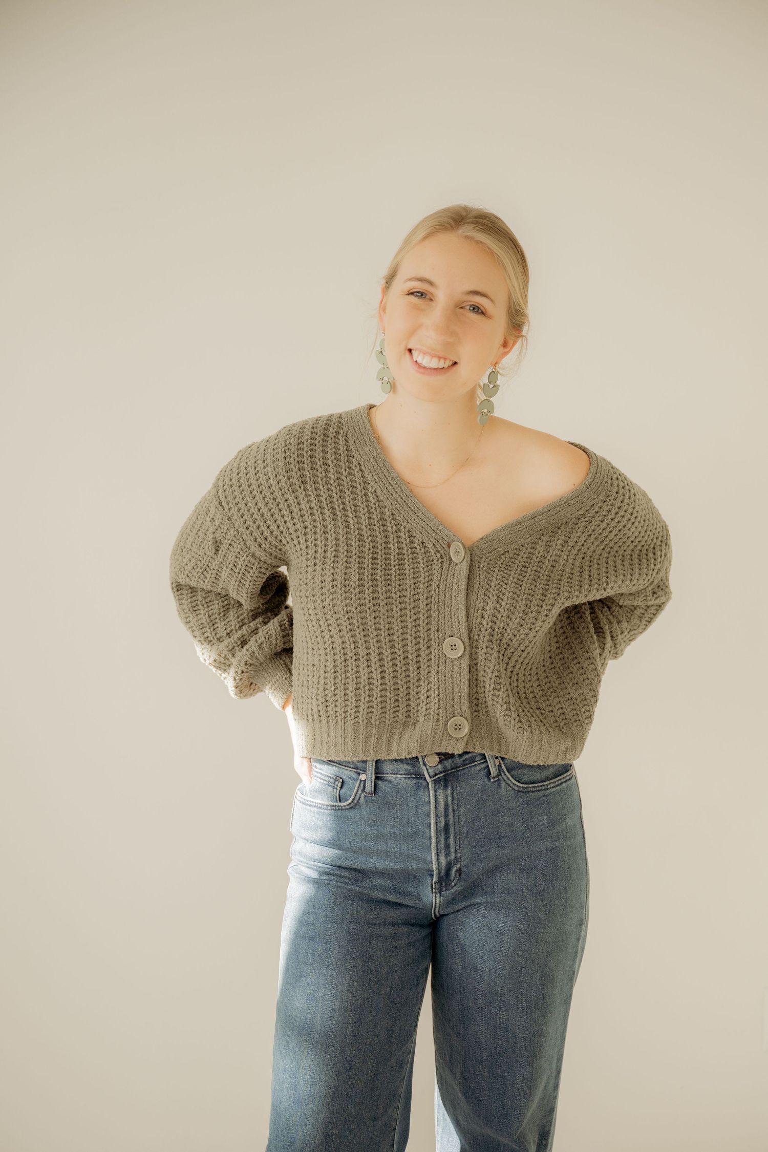 Person wearing oversized knit cardigan and high-waisted jeans poses against neutral background.
