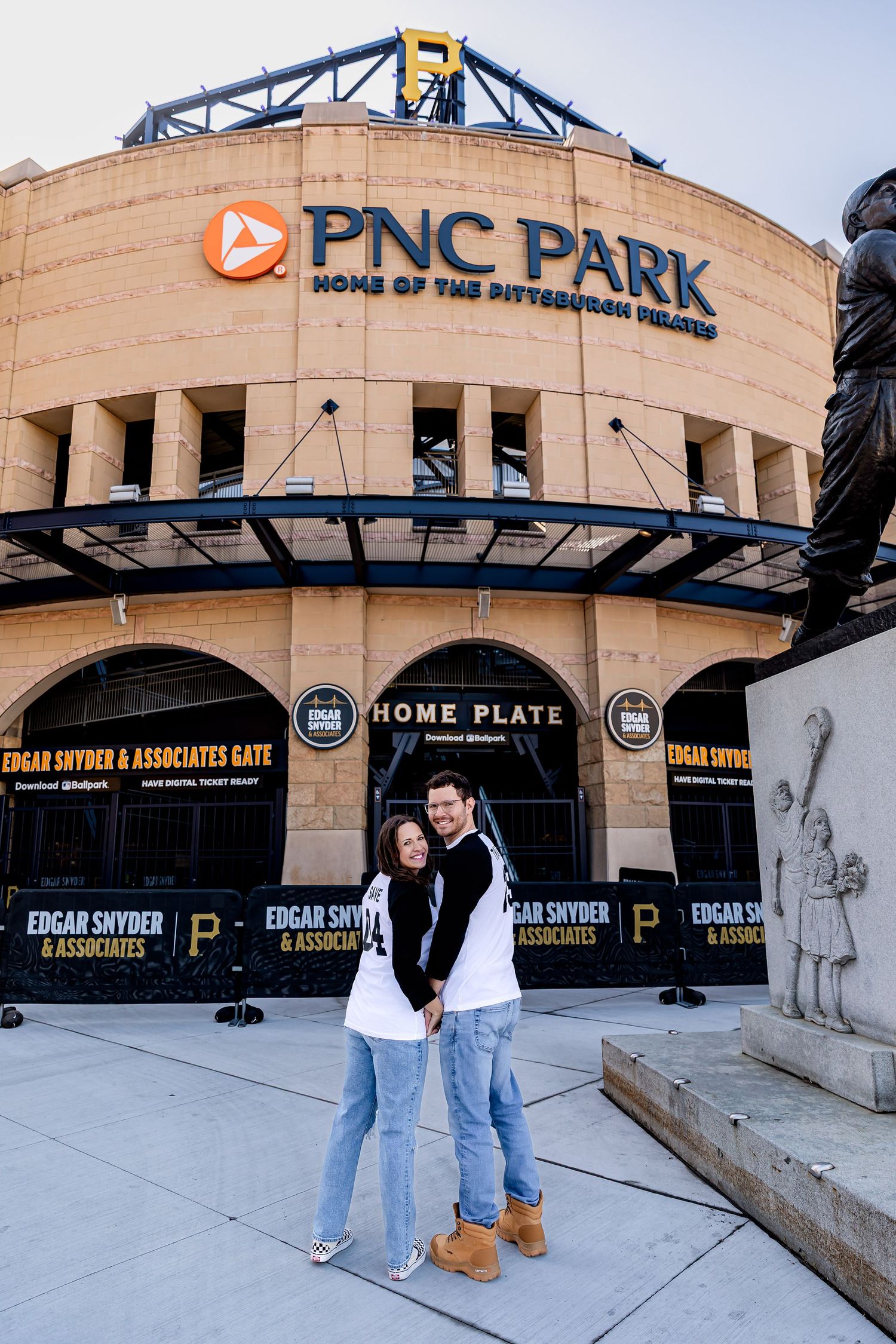 Baseball fans stand in front of PNC Park stadium entrance in Pittsburgh with iconic signage and architecture visible.