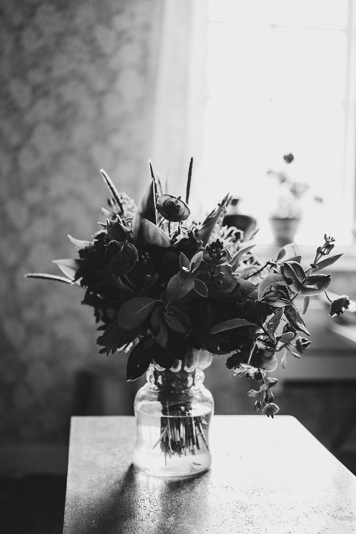 Vackert motljus över en brudbukett som står framför ett fönster. Bilden är svartvit med en soft kontrast, bröllopsfoto av Lets Bloom Media.