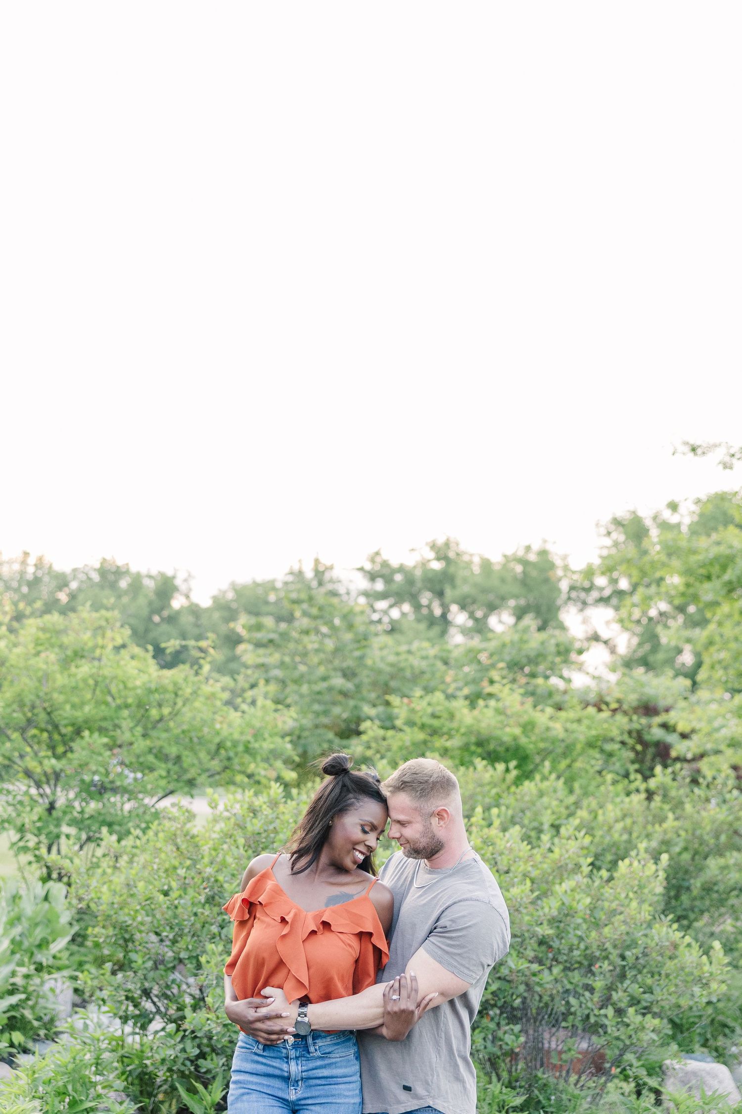 A couple share a joyful moment together outdoors among green foliage on a bright summer day.