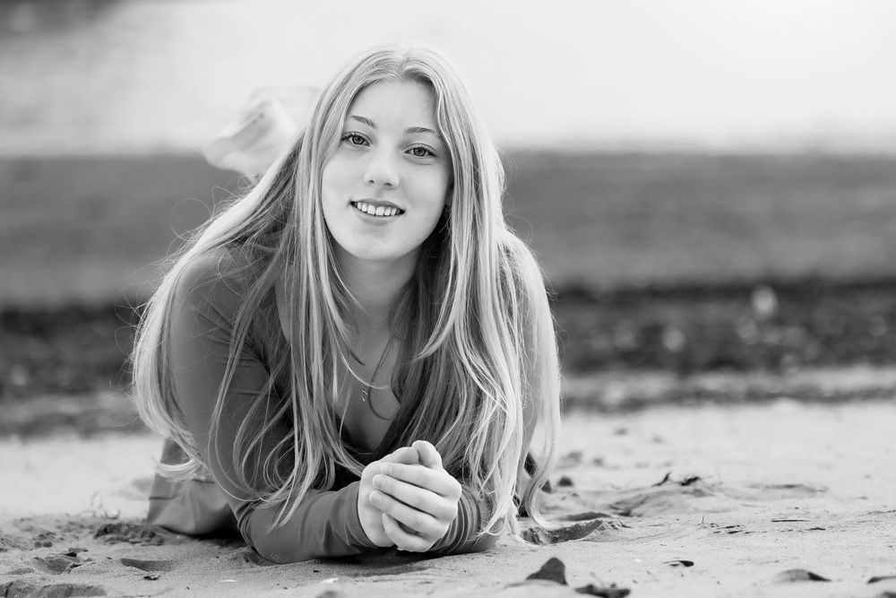 Black and white portrait of a person lying on sand at the beach with long blonde hair and relaxed expression.