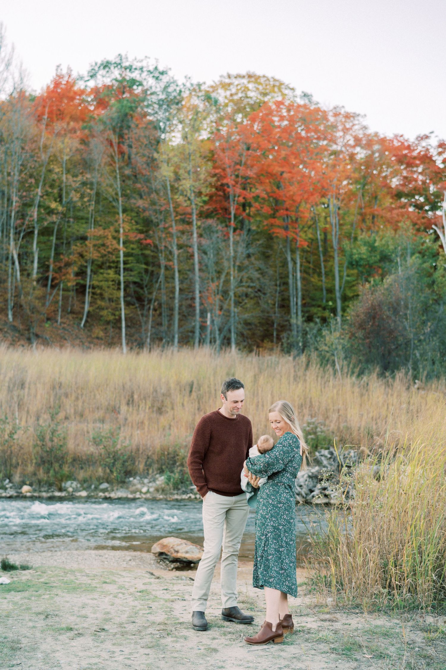 Couple enjoying a romantic autumn moment by a lake with colorful fall foliage in the background.