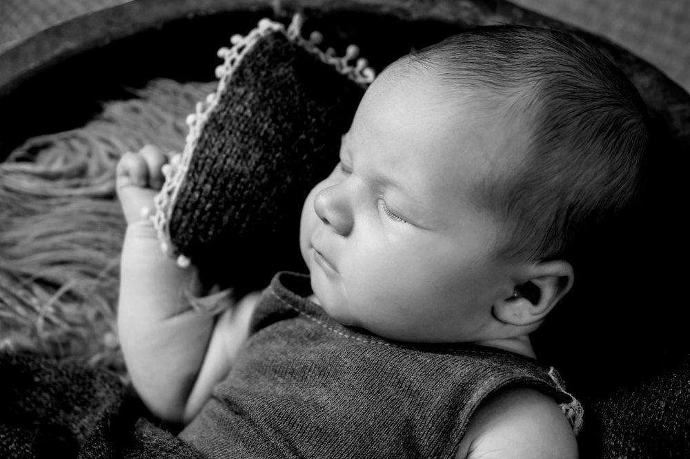 A sleeping baby in black and white photography lies peacefully against a textured blanket.