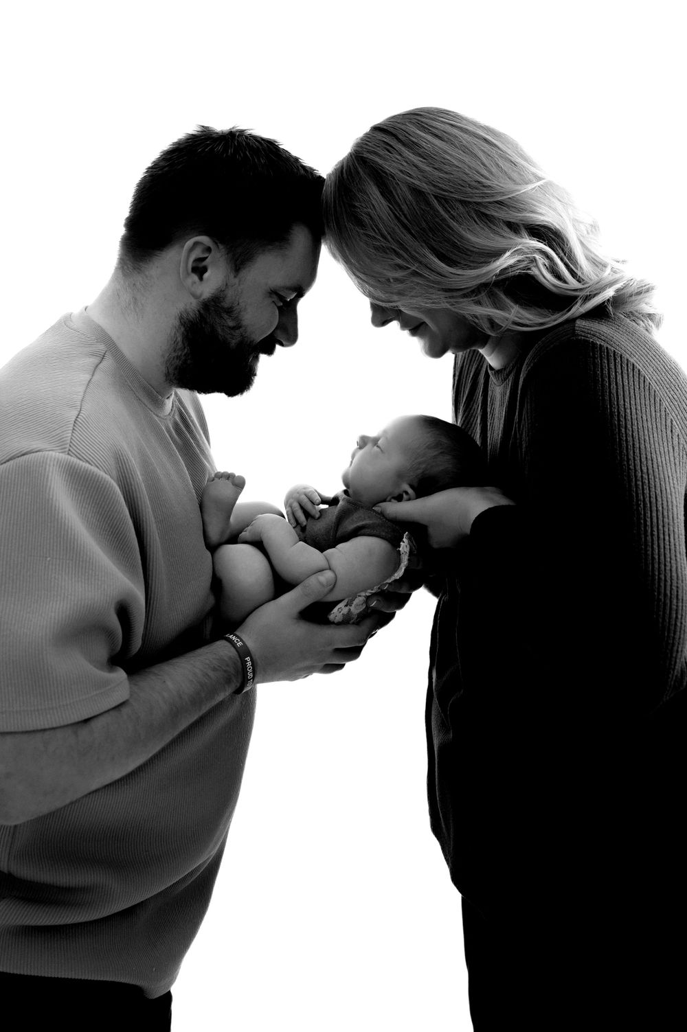 Black and white portrait of parents lovingly gazing down at their newborn baby in an intimate family moment.