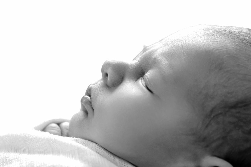 A peaceful black and white close-up of a baby sleeping soundly on soft bedding.