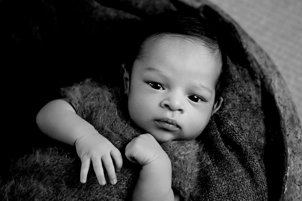 Black and white portrait of a small baby wrapped in a cozy dark blanket.