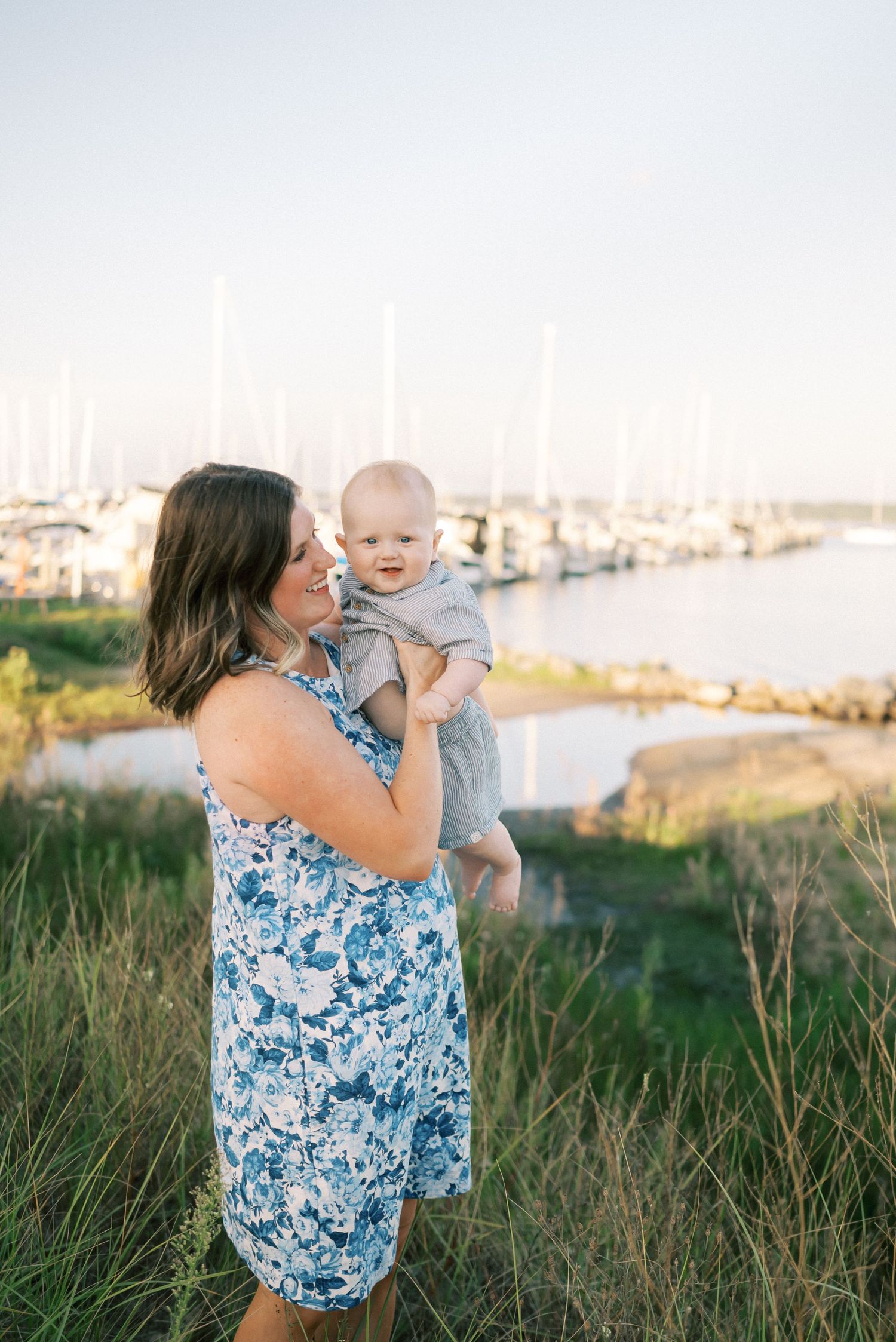 A sweet moment between parent and child standing by a marina with boats in the background at sunset.