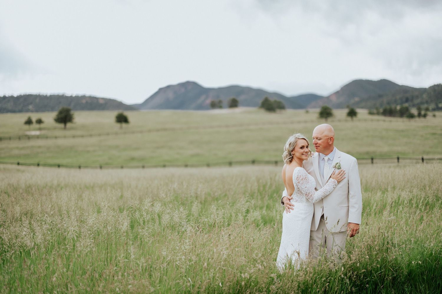 A couple in wedding attire shares a tender moment in a scenic mountain meadow with rolling hills in the background.