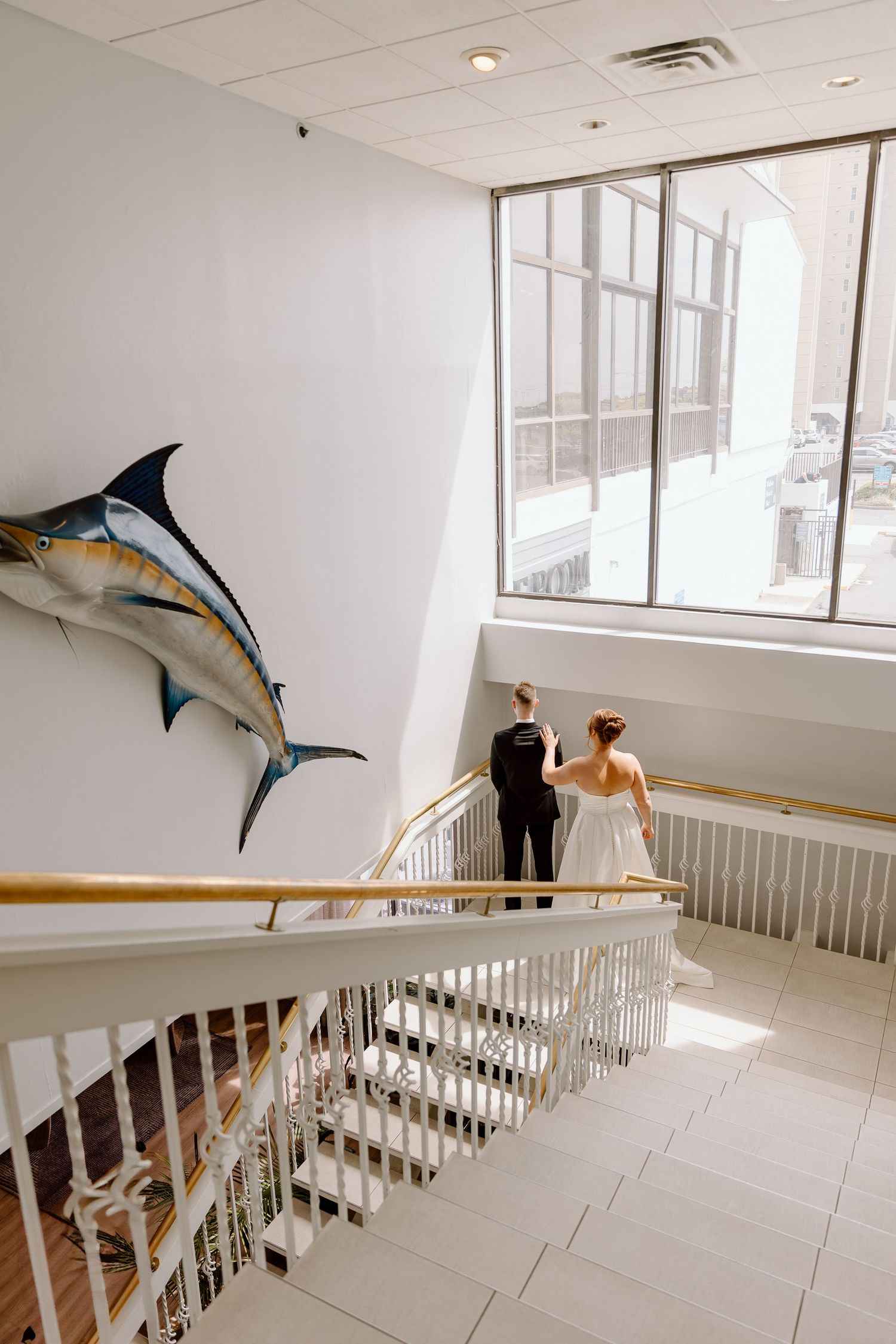 Someone releases flying kite-like sculptures in a modern gallery space with white walls and wooden railing.