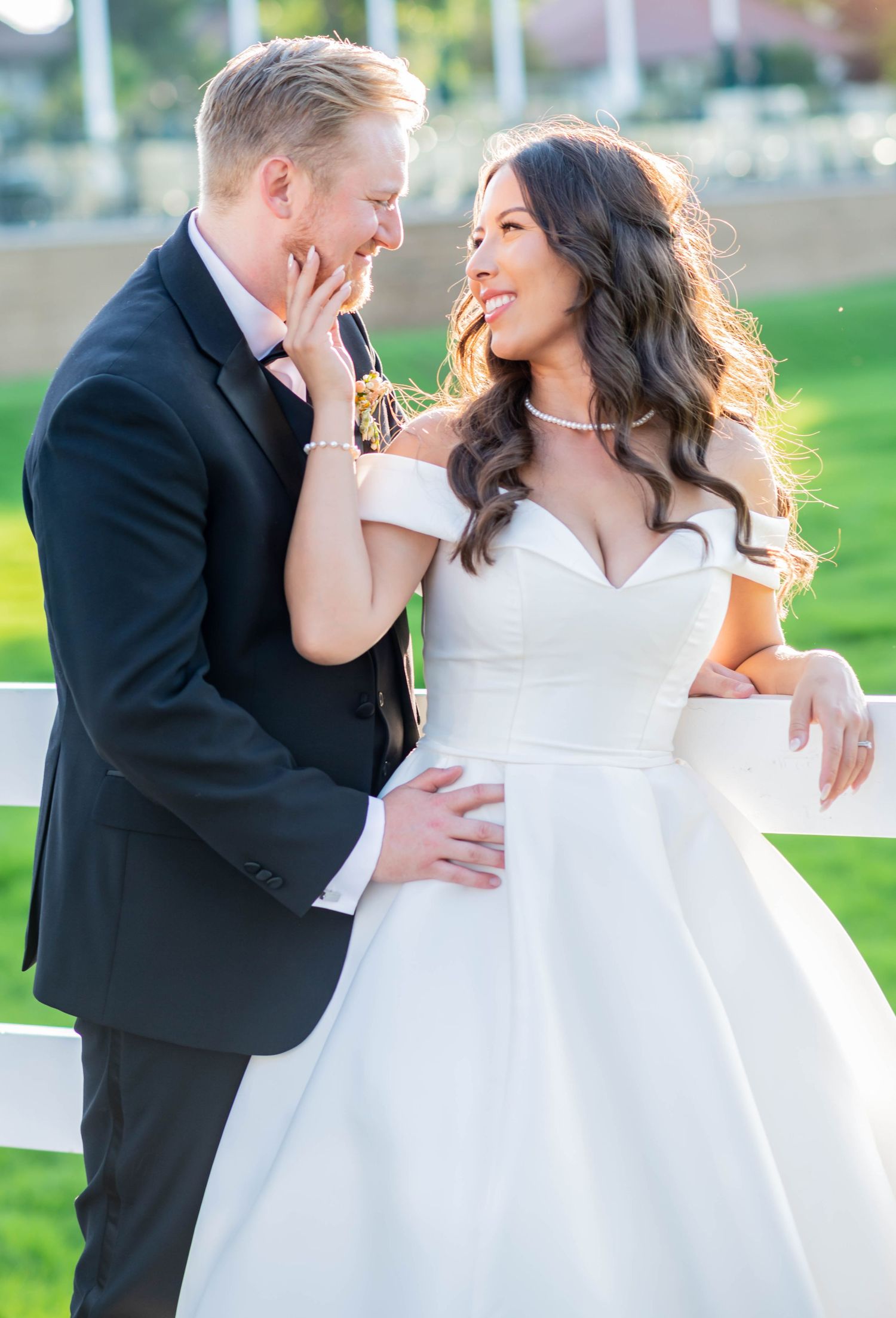 A joyful couple shares a candid laughing moment outdoors, with the bride wearing an elegant white off-shoulder gown.