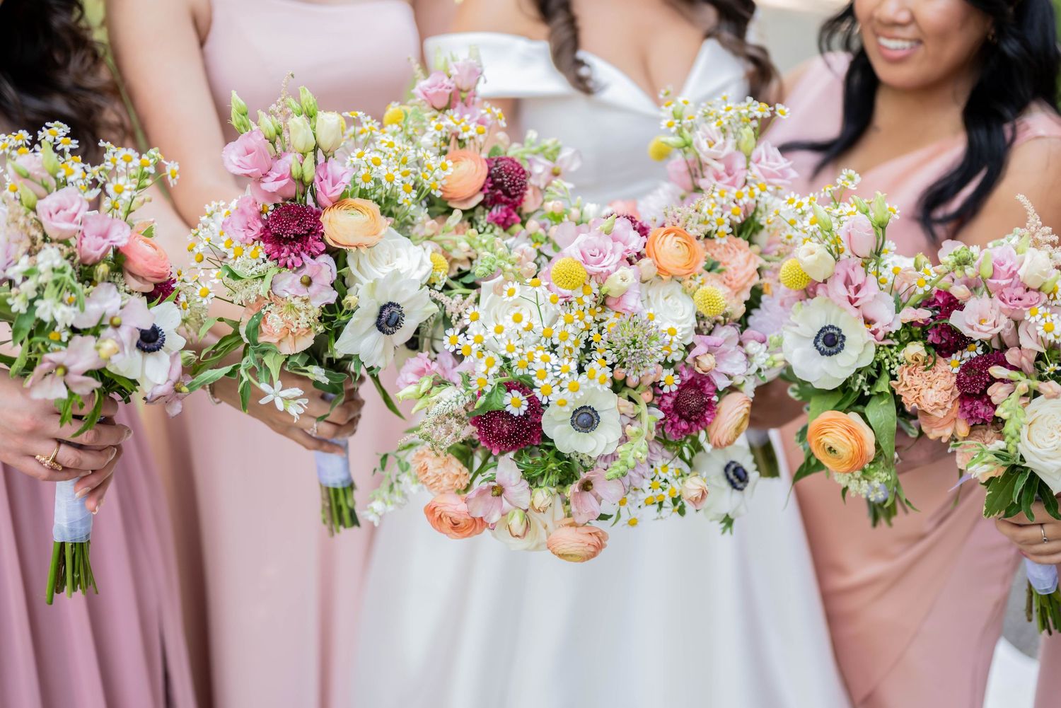 Close up of bridesmaids holding pink, burgundy and peach garden-style bouquets with anemones and wildflowers.