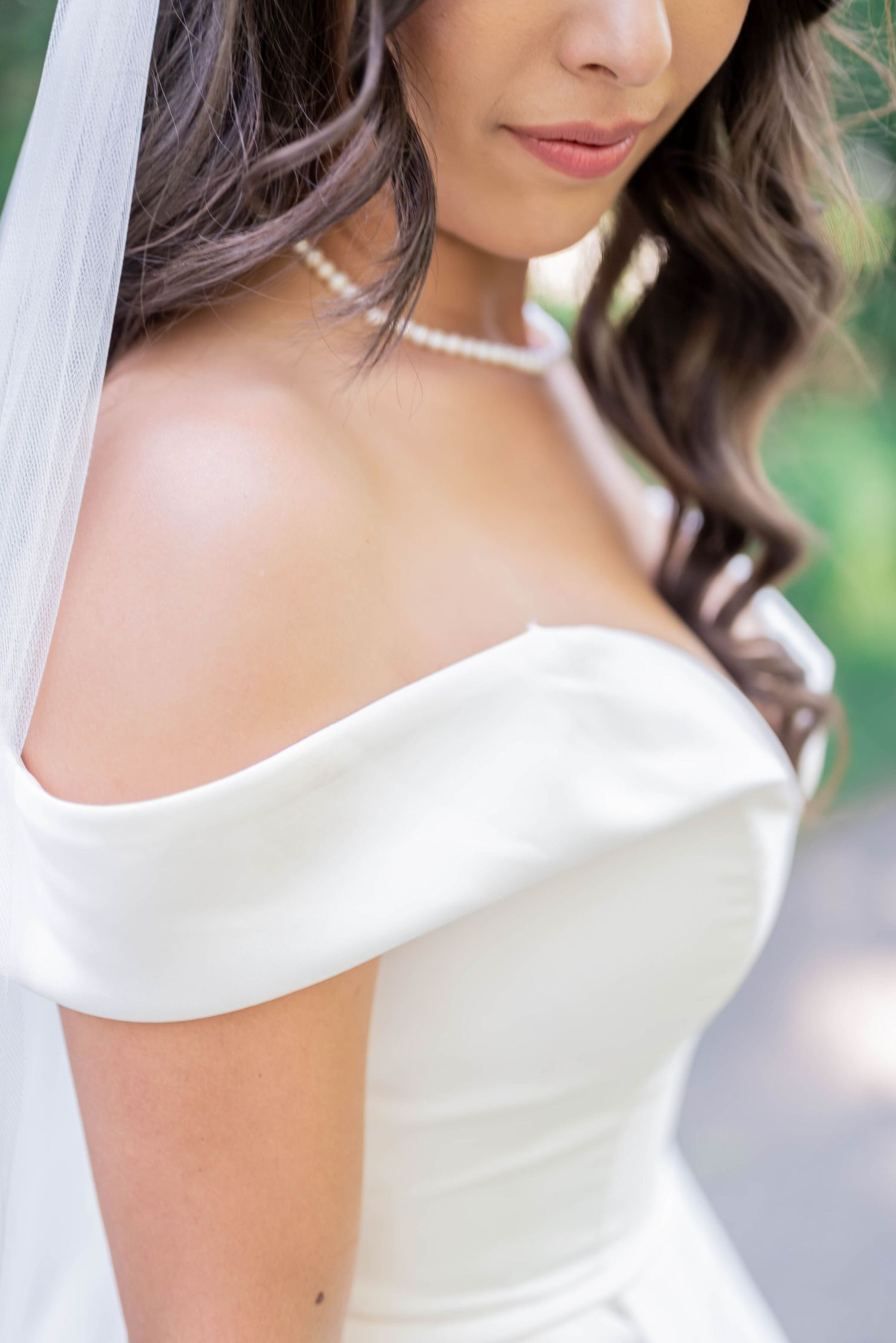 Close-up details of a classic white off-shoulder wedding dress with pearl necklace accessory.