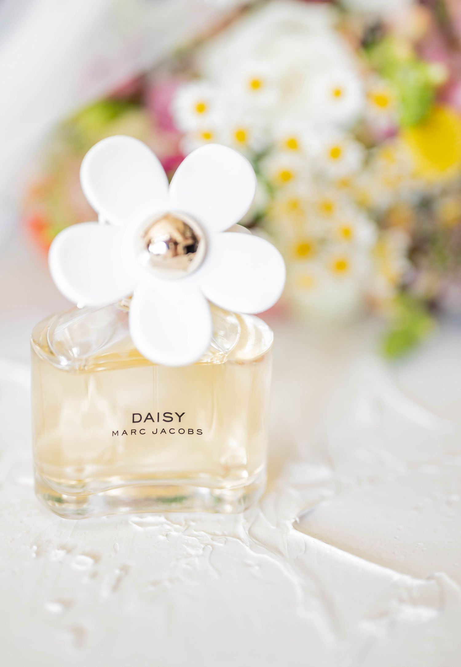 Close-up shots of Marc Jacobs Daisy perfume bottles with white floral cap design against soft blurred background.
