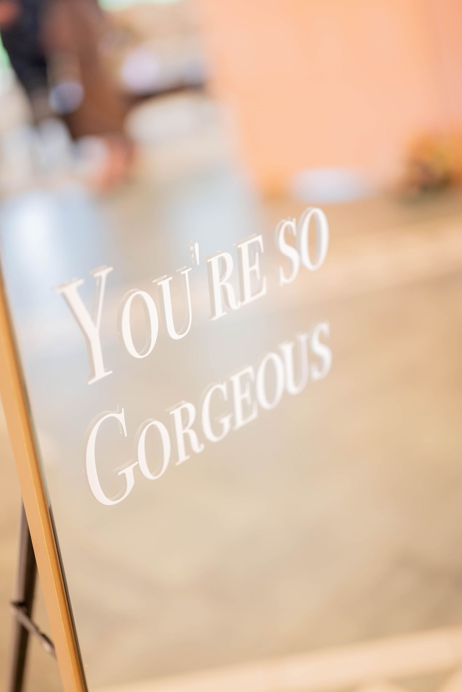 A wedding sign in delicate white script lettering displays 'You're So Gorgeous' against a blurred background.