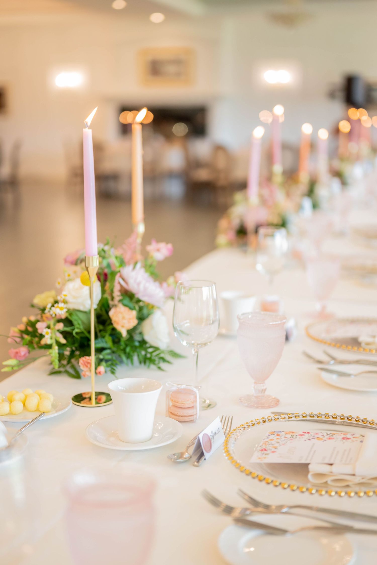 Elegant wedding reception table setting with gold charger plates, tall white candles, and delicate floral centerpieces.