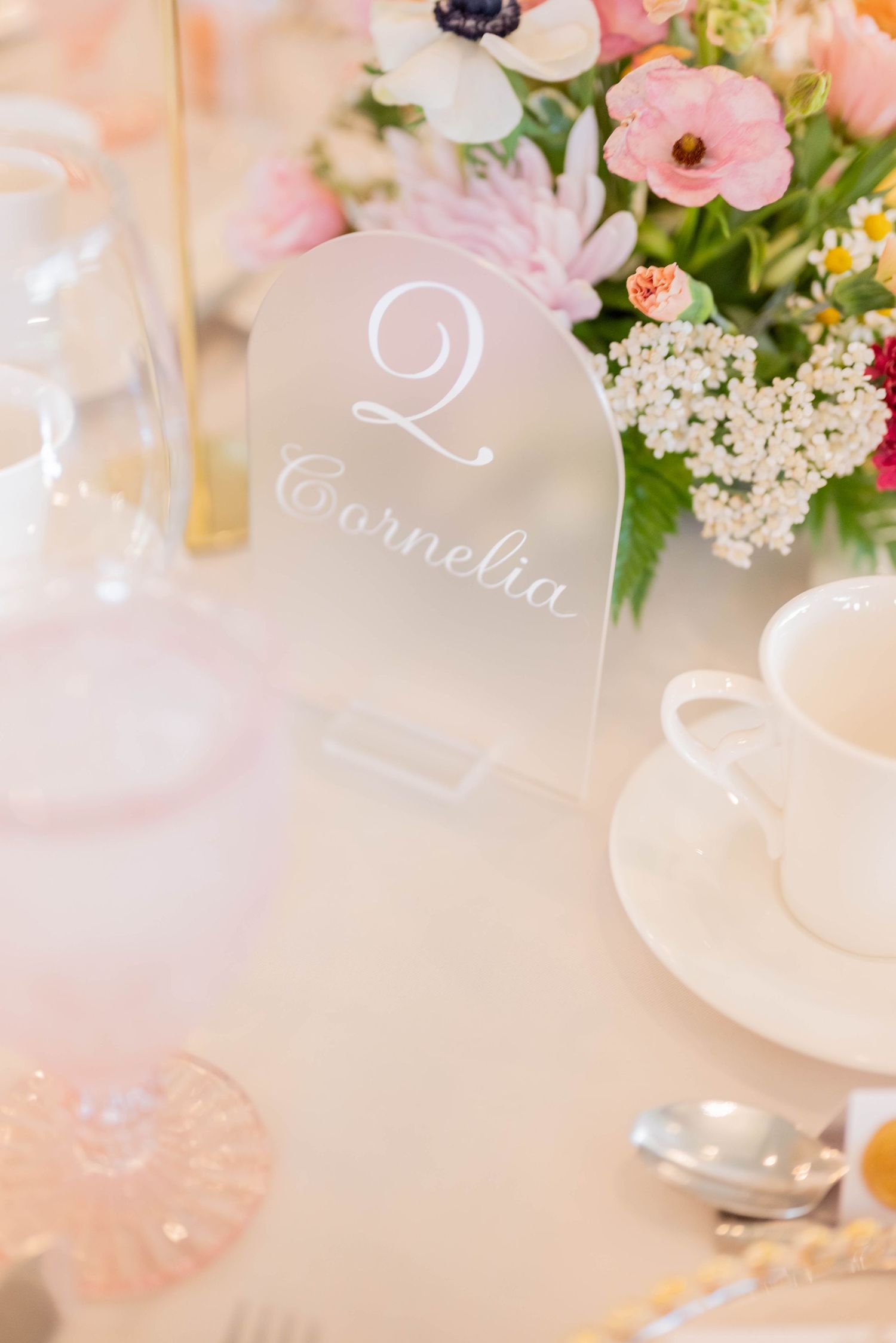 Elegant wedding table setting with soft pink ranunculus flowers, delicate table numbers, and white Queen Anne's lace.