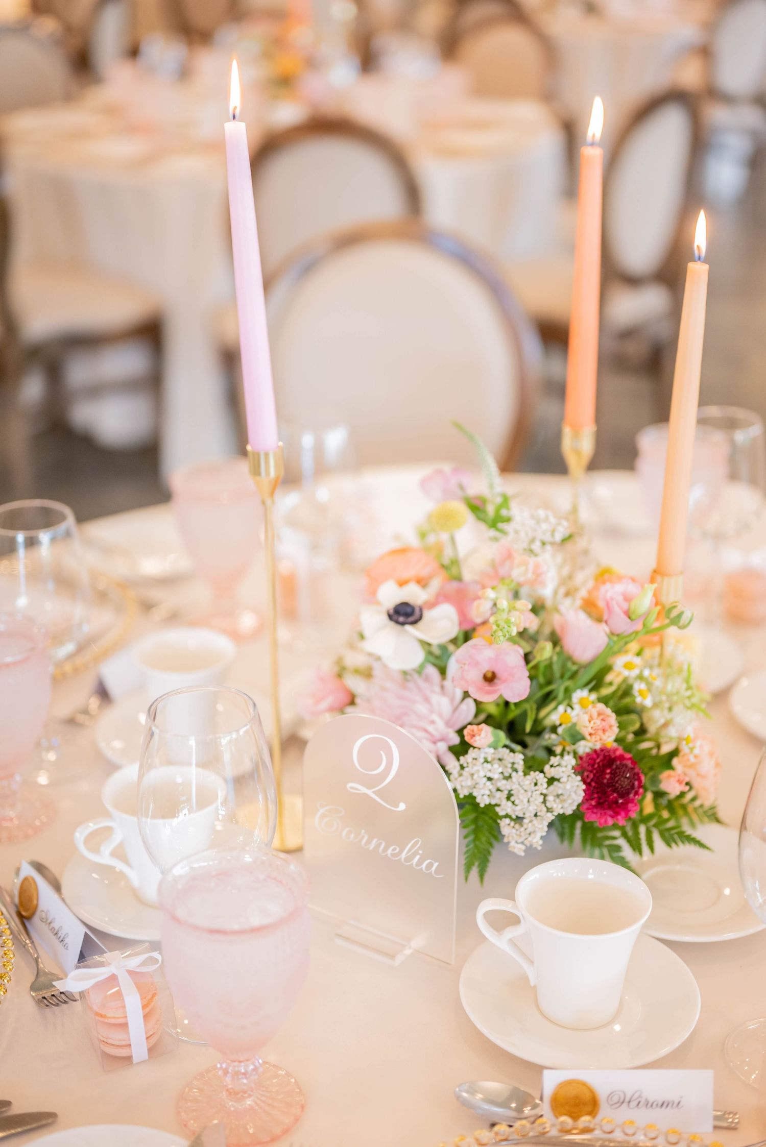 Romantic wedding table decor with lit candles, teacups, and pink floral arrangements on white linens.