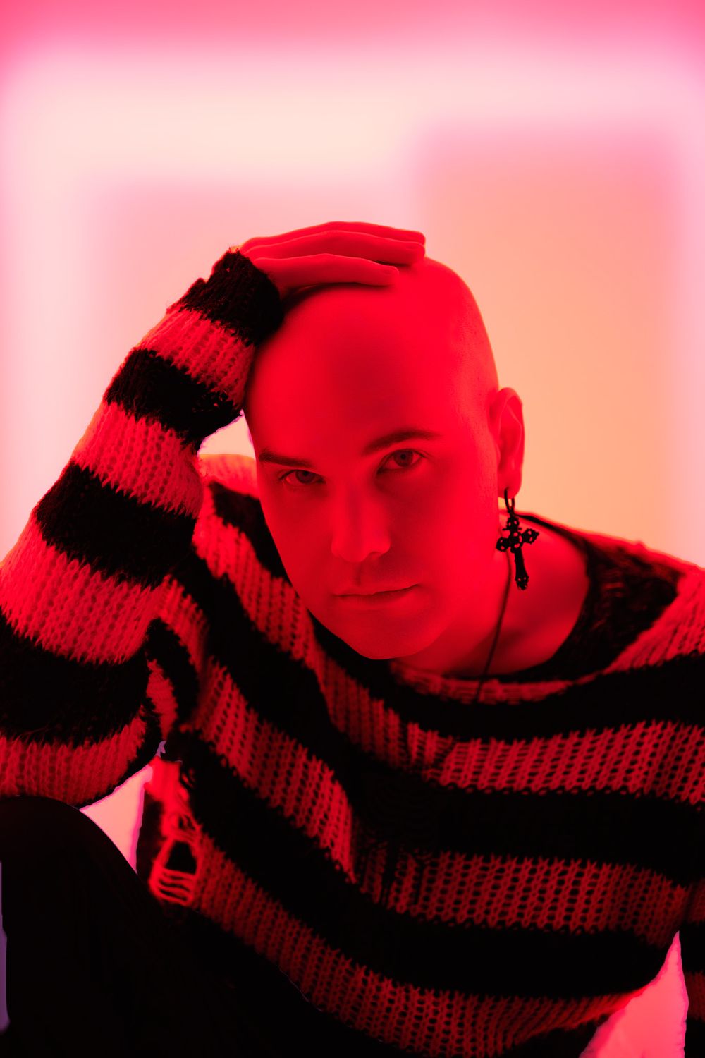 Studio portrait with red lighting featuring person in black and red striped sweater against pink background.