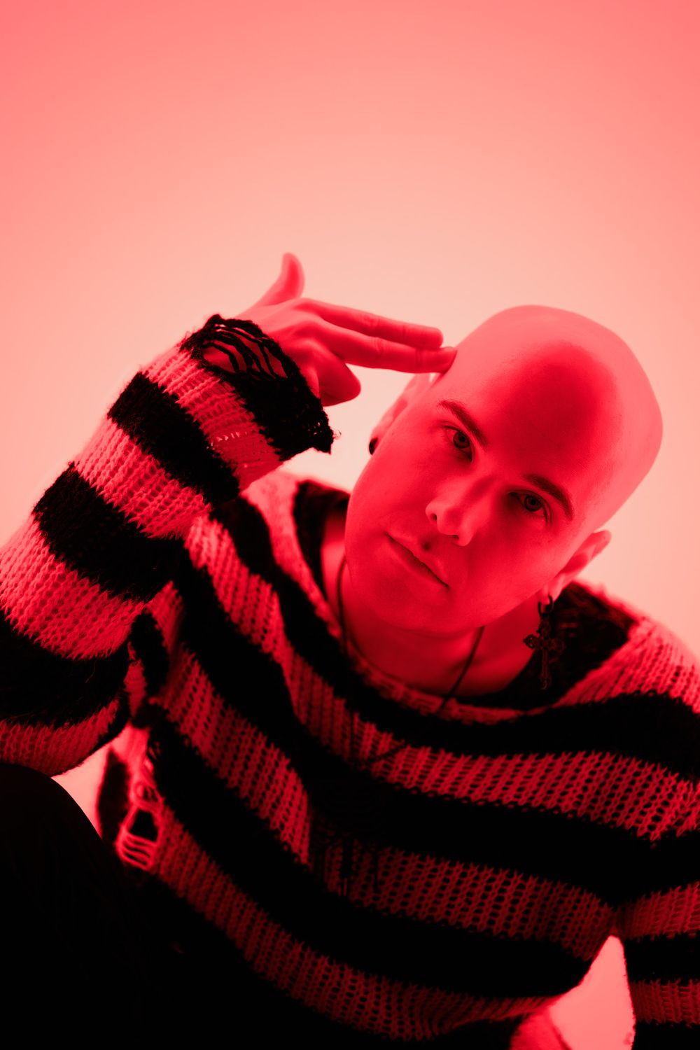 A face partially covered by a striped scarf or knit fabric shown in red monochromatic lighting.