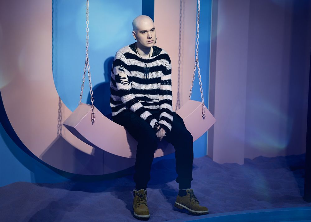 Figure in black and white striped sweater sits on pink geometric set piece against blue background.