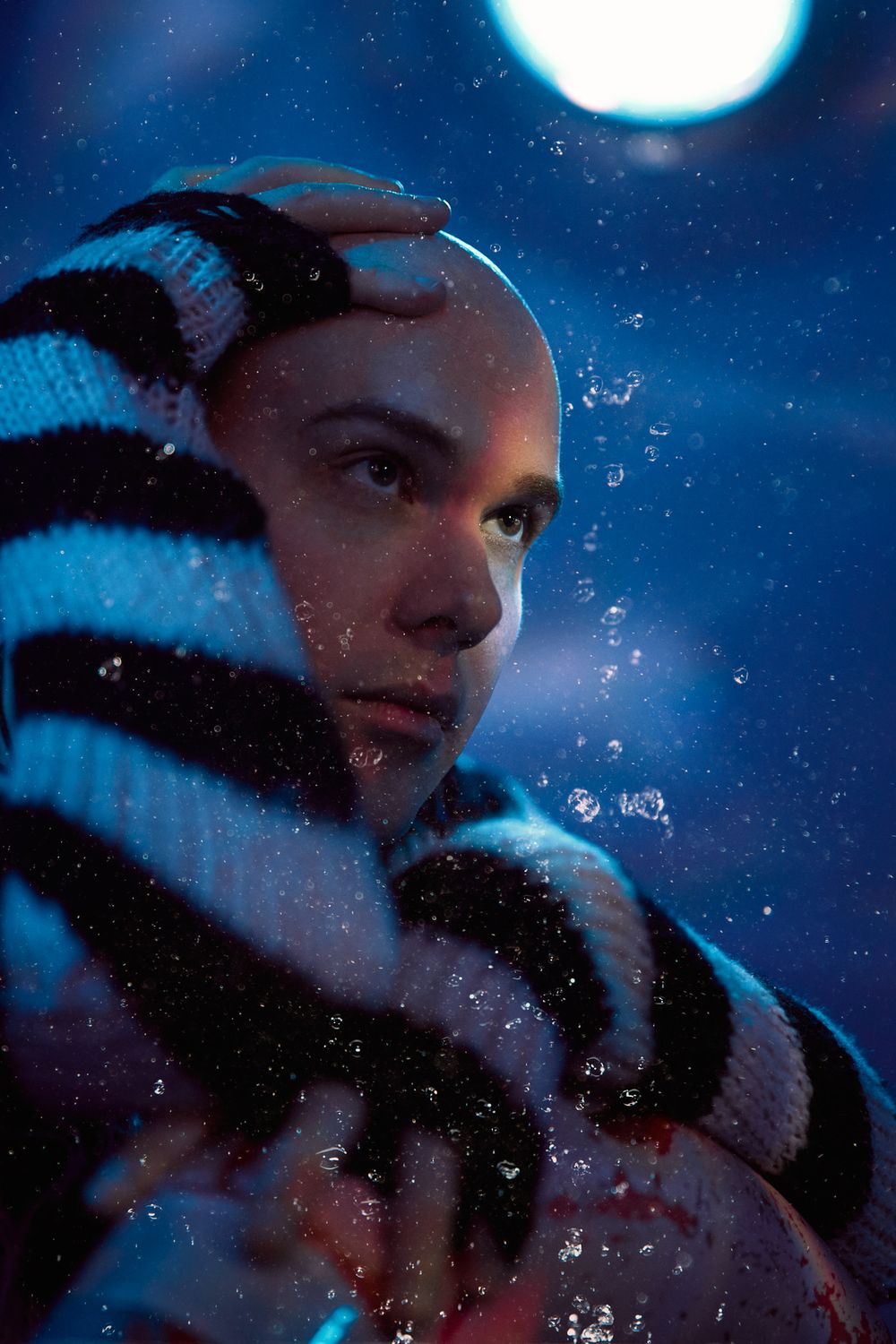 Moody nighttime portrait with striped scarf against starry sky and full moon in cool blue tones.