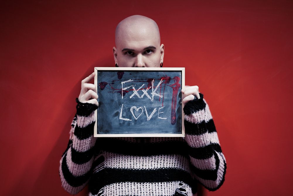 Person holding a chalkboard with fake love written on it against a red background while wearing a striped sweater.