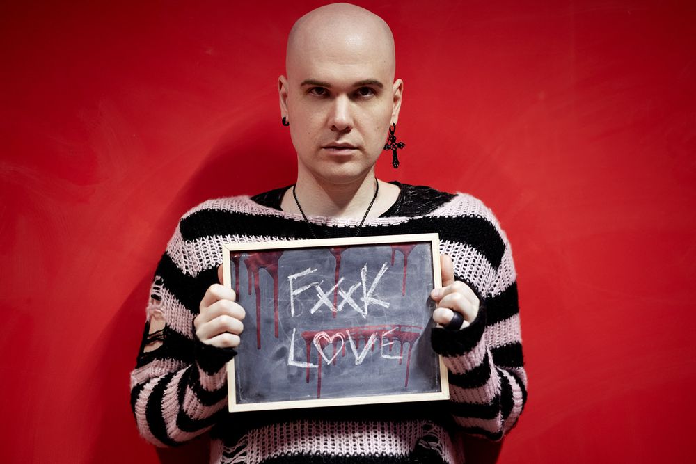 A person in a striped sweater holds up a chalkboard sign with text against a bright red background.