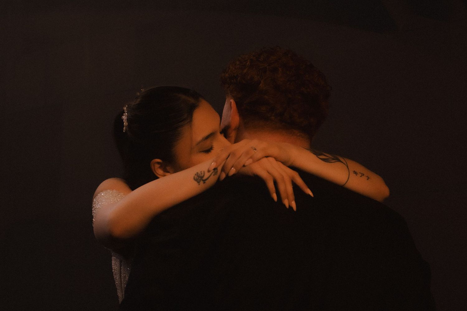 Natural photography as a couple embraces intimately in a dimly lit setting with warm ambient lighting and dark shadows.