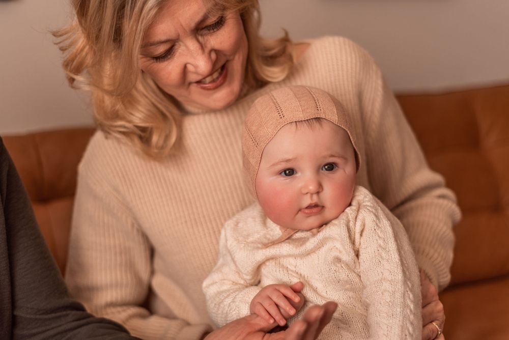 Joyful indoor portrait of a baby in knit clothes being held in warm natural lighting.
