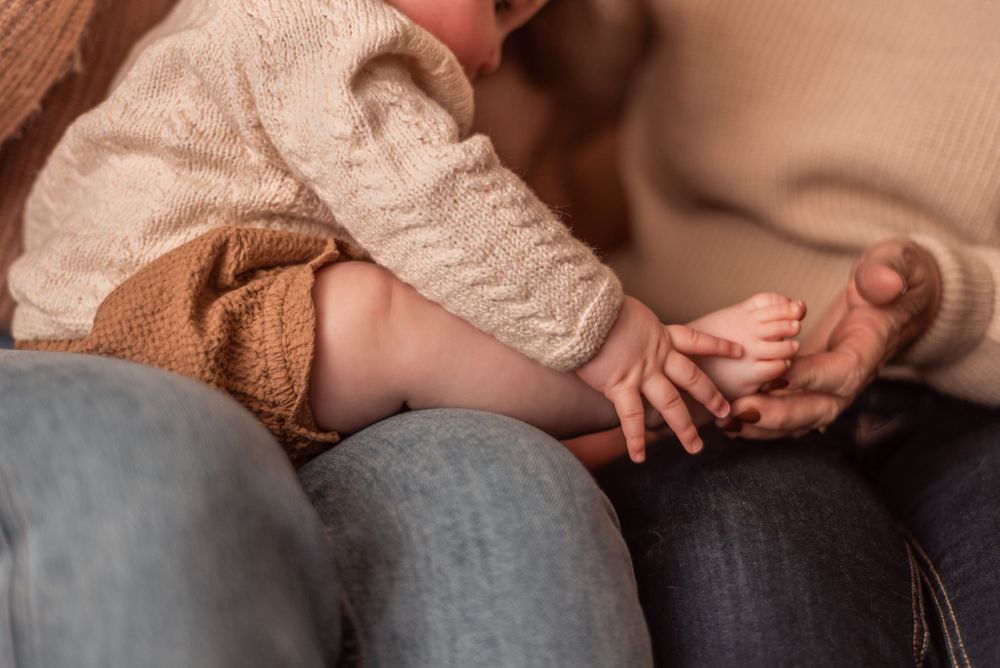 Baby's tiny feet rest on parent's lap in cozy close-up shot.