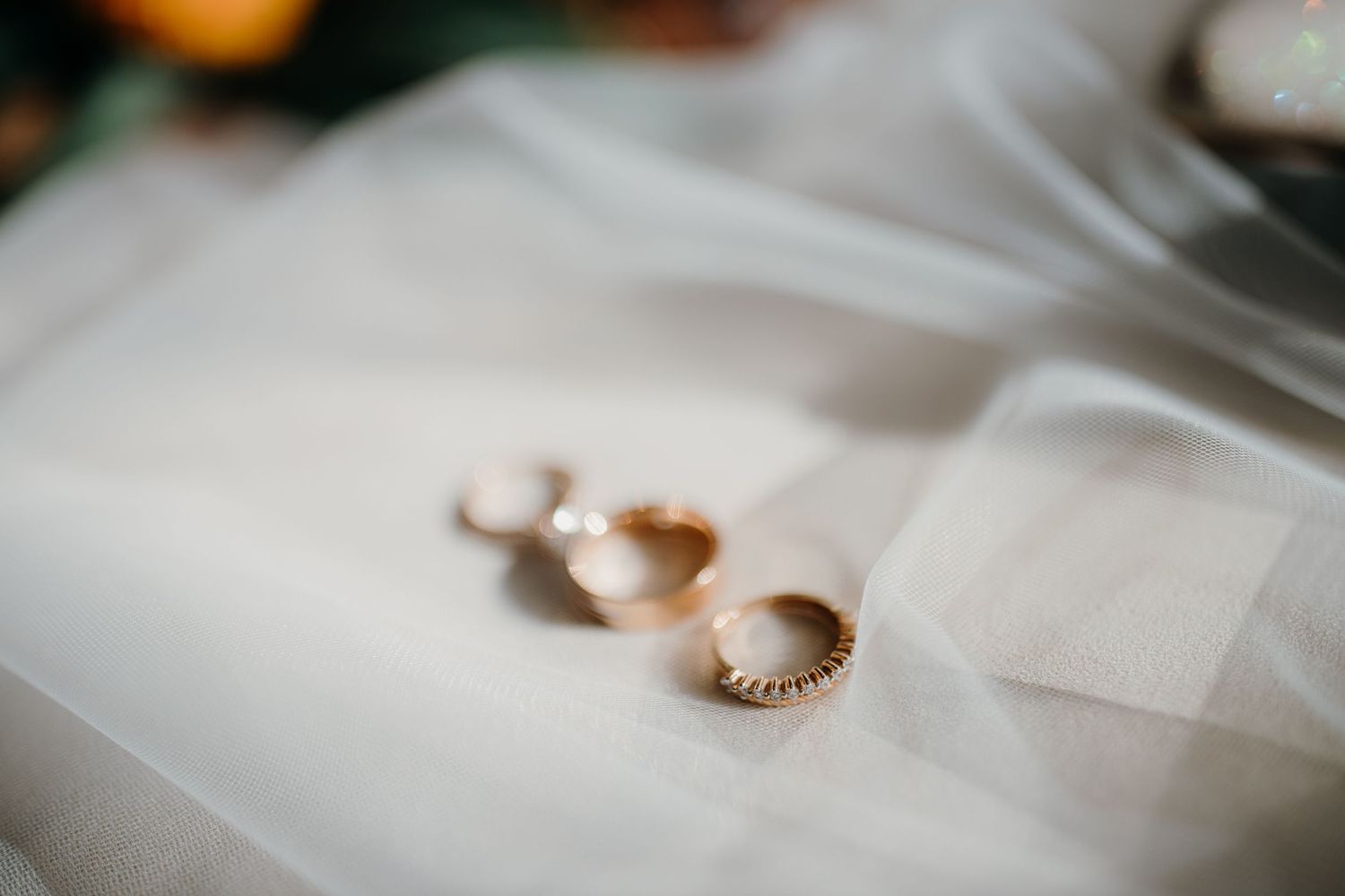 Gold wedding rings and engagement ring arranged on white fabric with soft focus and natural lighting.