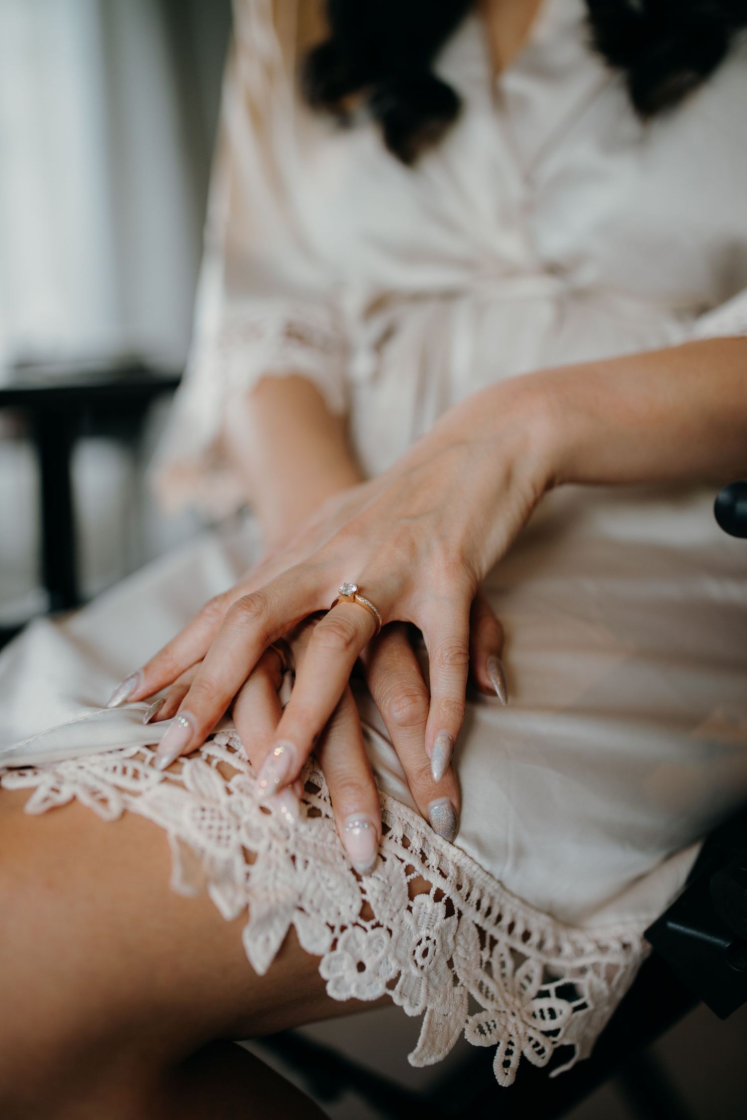 Close up of delicate lace trimming on white silk robe with a diamond ring on manicured hand.