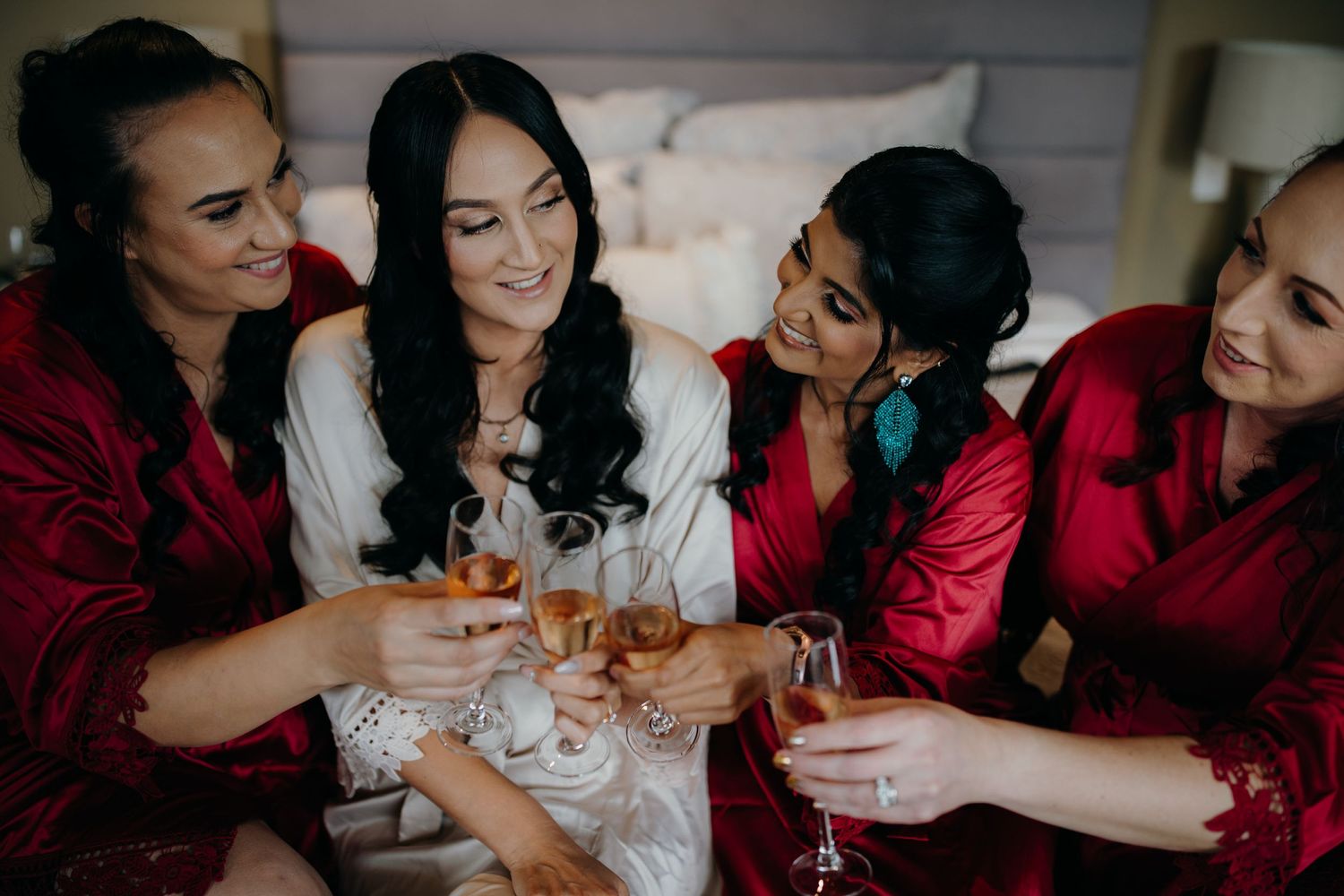 Wedding party wearing red and white satin robes toasting with champagne glasses in a celebratory moment.