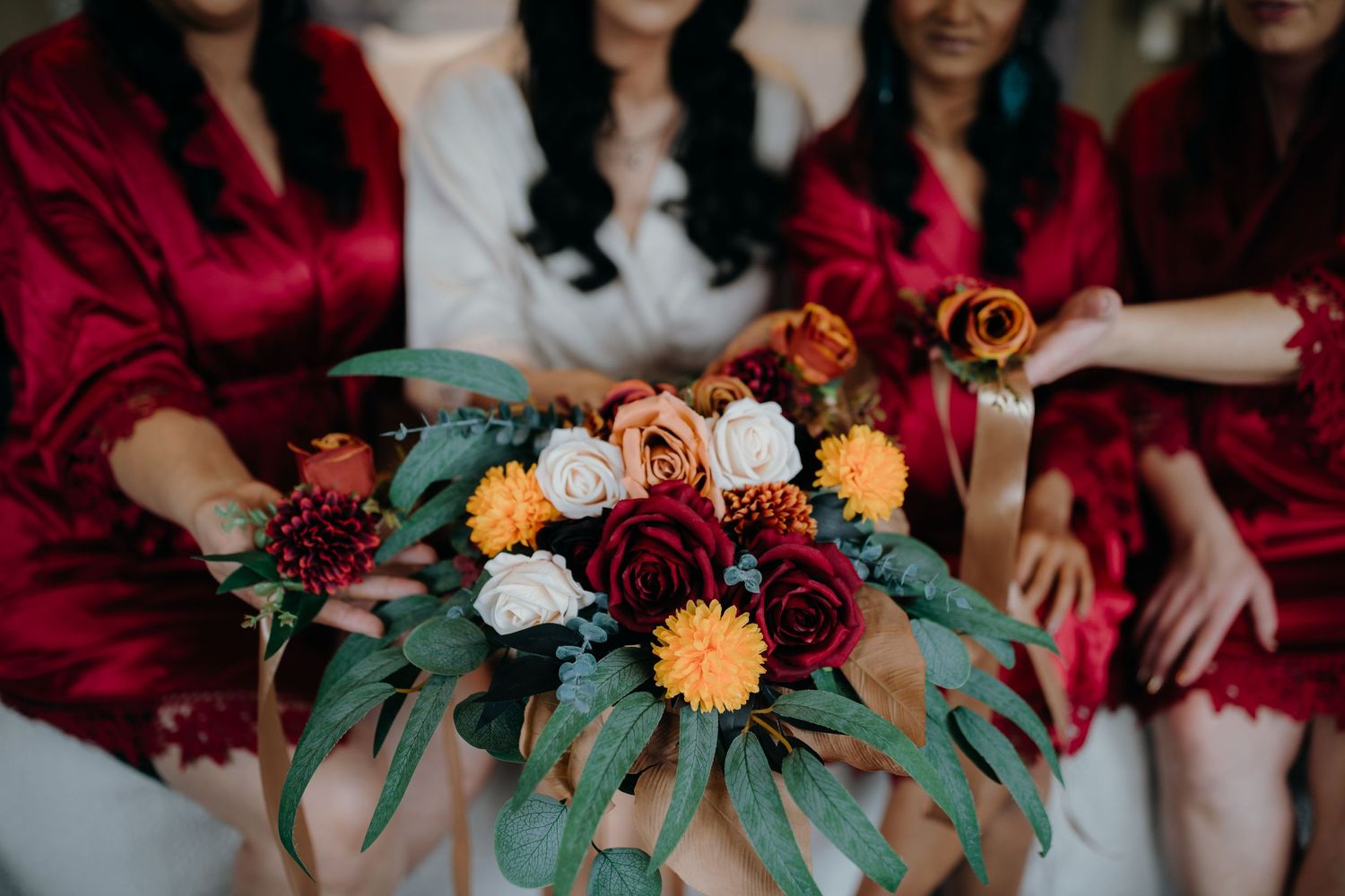 A vibrant wedding bouquet with deep red, peach and white flowers surrounded by eucalyptus leaves and red velvet.