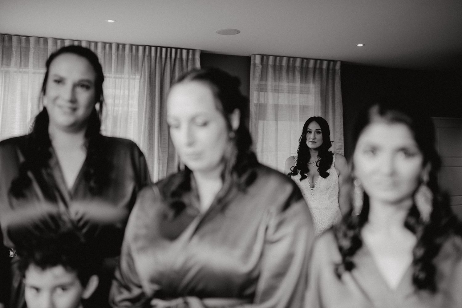 Black and white artistic wedding photo showing bridesmaids in satin dresses preparing for the ceremony.